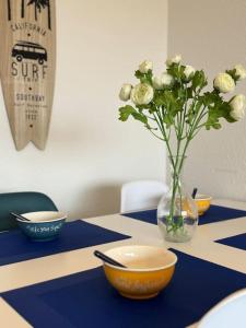 a table with bowls and a vase with flowers in it at Cozy apartment with balcony 1 minute from the sea / Appartement T2 cosy avec balcon à 1 min de l'océan in Capbreton