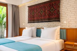 two beds in a hotel room with a painting on the wall at IZE Canggu by LifestyleRetreats in Canggu
