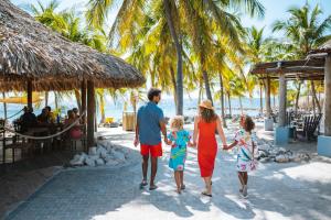 een familie wandelend op het strand met palmbomen bij Blue Bay Curaçao Golf & Beach Resort in Willemstad