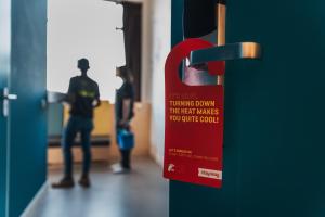 un panneau rouge sur une porte avec des personnes debout dans un couloir dans l'établissement Stayokay Hostel Texel, à Den Burg