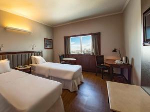 a hotel room with two beds and a desk and a window at Mercure Uberlândia Plaza Shopping in Uberlândia