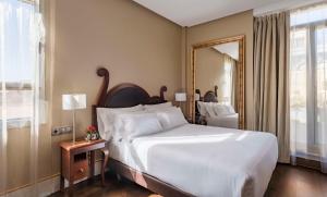 um quarto com uma grande cama branca e um espelho em NH Collection Madrid Paseo del Prado em Madri