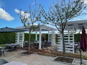 une pergola blanche avec des tables, des chaises et des arbres dans l'établissement Brit Hotel La Bonne Etape, à Évreux