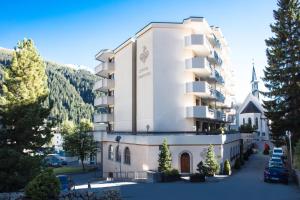 a large white building with a church in a parking lot at Central Sporthotel Davos in Davos