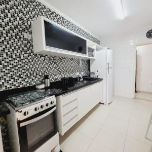 Biała kuchnia z kuchenką i lodówką w obiekcie Apartarmento Ar Con - WIFI - Garagem - Piscina - Enseada Guarujá w mieście Guarujá