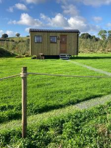 a small green building in a field with a fence at Shepherd's Huts in Barley Meadow at Spring Hill Farm in Oxford