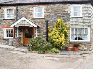 een stenen huis met een bruine deur en een aantal planten bij Mill Cottage in Liskeard