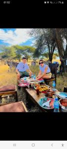 deux personnes assises à une table de pique-nique devant les zèbres dans l'établissement Rainbow house, à Boma la Ngombe