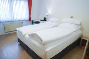 1 dormitorio con 1 cama grande con sábanas y almohadas blancas en AP Hotel Viernheim Mannheim am Kapellenberg, en Viernheim