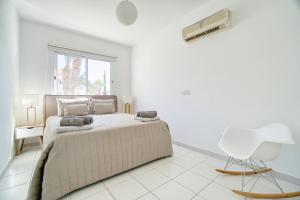 een witte slaapkamer met een bed en een witte stoel bij Iris Village Block 12-105 in Paphos City