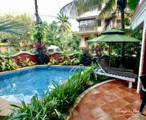 a swimming pool with a bench and an umbrella at Renzo's Inn in Calangute