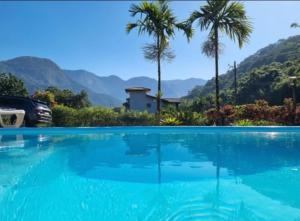 a large blue swimming pool with palm trees and mountains at Casa rosa de Guapimirim in Guapimirim