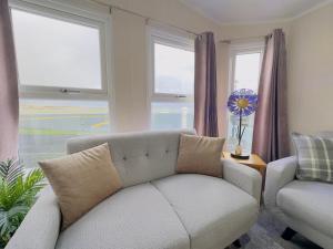 een woonkamer met een bank, een stoel en ramen bij LakeDistrict Caravan by Sleepy in Millom