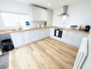 a kitchen with white cabinets and a wooden floor at Blossom Holiday Lets - 96 Roseberry Cottages in Guisborough