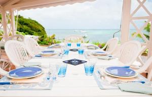 - une table blanche avec des assiettes et des verres et l'océan dans l'établissement Villas Cap Est OFFRE SPECIALE PONT DE MAI 1 NUIT OFFERTE, au François