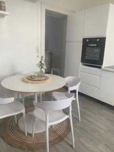 a white kitchen with a table and white chairs at Charmante petite maison in Maubeuge