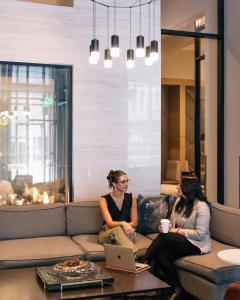 Dos mujeres sentadas en un sofá con un portátil en AC Hotel by Marriott Denver Downtown, en Denver