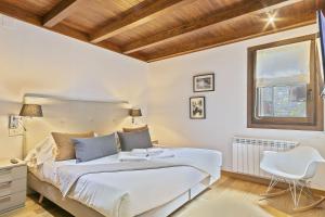 a white bedroom with a bed and a chair at Luderna - Apartamento Val de Ruda B15 Baretja in Baqueira-Beret