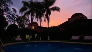 una puesta de sol sobre una casa con piscina y palmeras en Casa Shambhala Malinalco en Malinalco