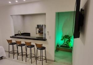 una cocina con 4 taburetes y una pared verde en Ressurgência loft, en Arraial do Cabo