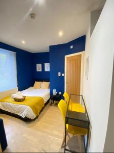 1 dormitorio con paredes azules, 1 cama amarilla y escritorio en En-suite near Stratford in a guesthouse, en Londres
