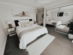 a white bedroom with a large bed and a mirror at Diggers Beach Villa Coffs Harbour in Coffs Harbour