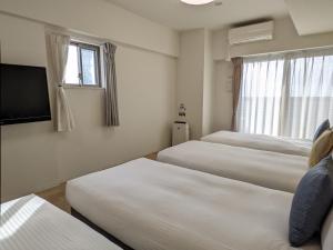 a hotel room with three beds and a television at ESLEAD HOTEL Namba South Ⅲ in Osaka
