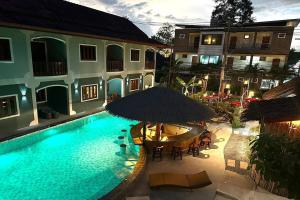 an outdoor swimming pool with an umbrella and tables and chairs at Ginis Beach Resort in Kamala Beach