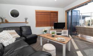 een woonkamer met een zwarte leren bank en een tafel bij Beachfront Bliss On Wanaka Terrace Support Local in New Plymouth