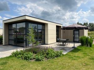 un edificio con una mesa y una sombrilla en Marina Strandbad Chalet Aan het Strand mit Zaun Haus Nr 133, en Olburgen