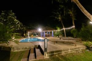 una piscina por la noche con una mesa y bancos en Namsai Resort Kanchanaburi, en Kanchanaburi