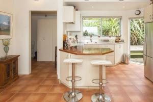 a kitchen with white cabinets and a counter with stools at Chester Cottage Beachfront in Oakura