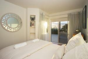 a white bedroom with a bed and a large window at Chester Cottage Beachfront in Oakura