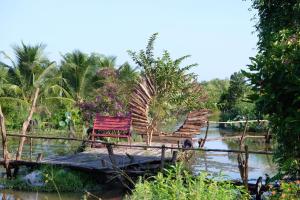 a red bench sitting on a bridge over a river at Bungalow - Farmstay Hoa Rừng U Minh in Cà Mau