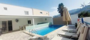 a swimming pool with chairs and an umbrella next to a house at Villa Oniro- Less than 5-Min Walk to Kalivaki Beach in Georgioupolis