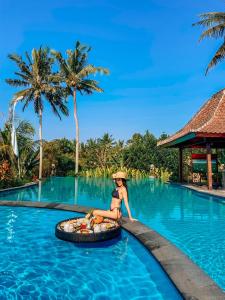 a woman in a hat sitting on a pool at a resort at Uma Dawa Resort and Spa in Ubud