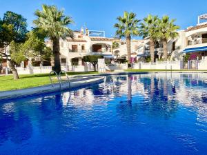 a large swimming pool with palm trees and a building at Gound Floor Bungalow Jumilla III Playa Flamenca in Orihuela Costa