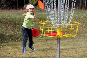 a young girl throwing frisbees into a yellow basket at Ramybės parkas 