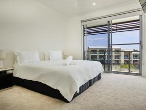 a white bedroom with a large bed and a large window at Emerald lakes 3 level villa in Gold Coast
