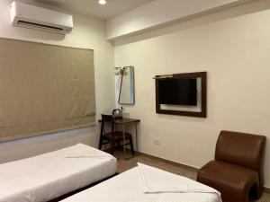 ein Hotelzimmer mit 2 Betten, einem Stuhl und einem TV in der Unterkunft Flora Embassy in Chennai