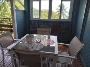 een glazen tafel en stoelen op een veranda bij LES GÎTES DU DOMAINE DE PETITE-ANSE in Bouillante