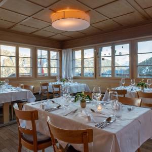 une salle à manger avec des tables blanches, des chaises et des fenêtres dans l'établissement Hotel Restaurant Capricorns, à Wergenstein