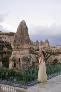 Aza Cave Cappadocia Adult Hotel في غوريمِ: امرأة ترتدي ثوب أصفر تقف على جسر تطل على جبل