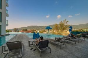 um grupo de pessoas sentadas em cadeiras ao lado de uma piscina em Sea view apartment at Oceana by Lofty em Kamala Beach