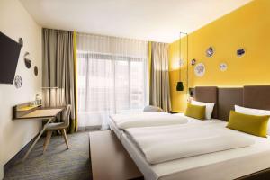 a hotel room with two beds and a desk at Vienna House Easy by Wyndham Berlin Prenzlauer Berg in Berlin