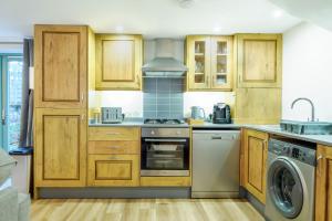 cocina con armarios de madera, lavadora y secadora en Porthallow, en Budock Water