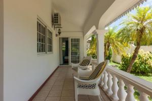 a porch of a house with two chairs and palm trees at Villa Confort in Grand'Anse Praslin