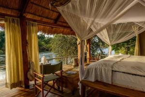 ein Schlafzimmer mit einem Himmelbett und einem Schreibtisch mit einem Stuhl in der Unterkunft Sindabezi Island Camp in Simonga