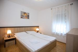 Cama blanca en habitación con ventana en Apartments Maslina I en Njivice