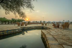 a pool of water with chairs and a sunset in the background at Tripli Hotels Stay Inn Resort Jaisalmer in Sām